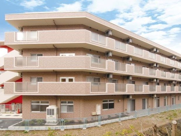エントランスの扉には、自動ドアが採用されている。壁には、郵便受けが設置されている。左側に数種類の花が植えられたプランターが置かれている。