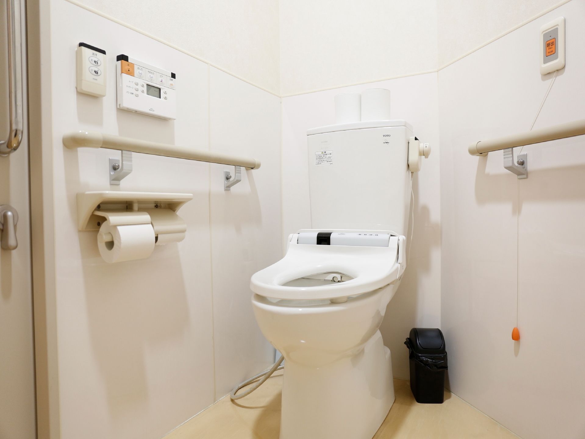 やや変則的な形の部屋のトイレ。左右に手すりはありナースコールも設置されている。部屋の壁は白い色をしている。