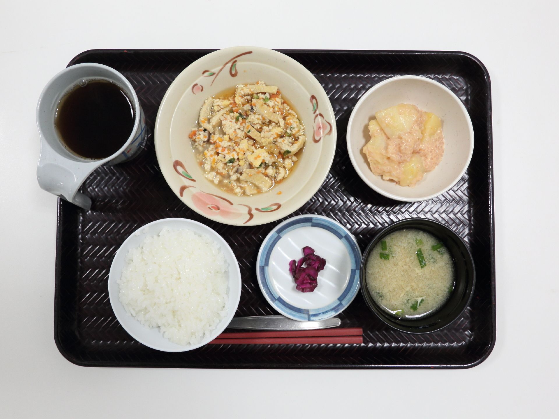 黒色のトレーにご飯とお味噌汁、メインおかずに小鉢が1つ、お漬物とお茶が添えてある。品数と栄養バランスが考慮された献立になっている。