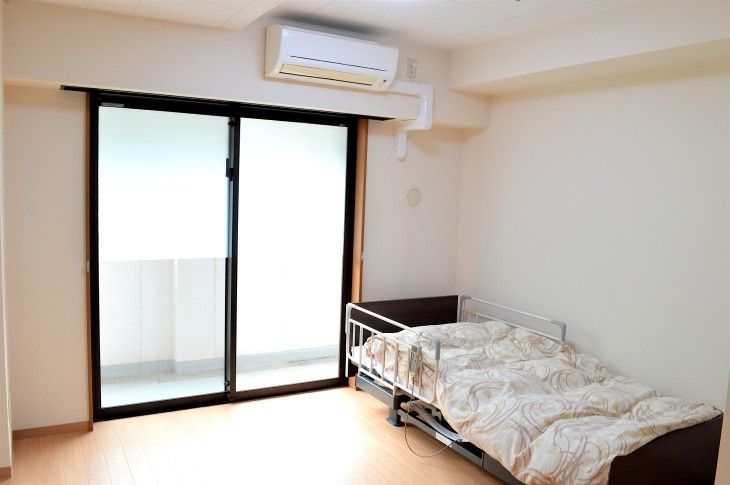 幅広い引き戸の出入口から右側には、トイレスペースになっている。壁際には電動ベッドが置いてあり、ナースコールが設置してある。