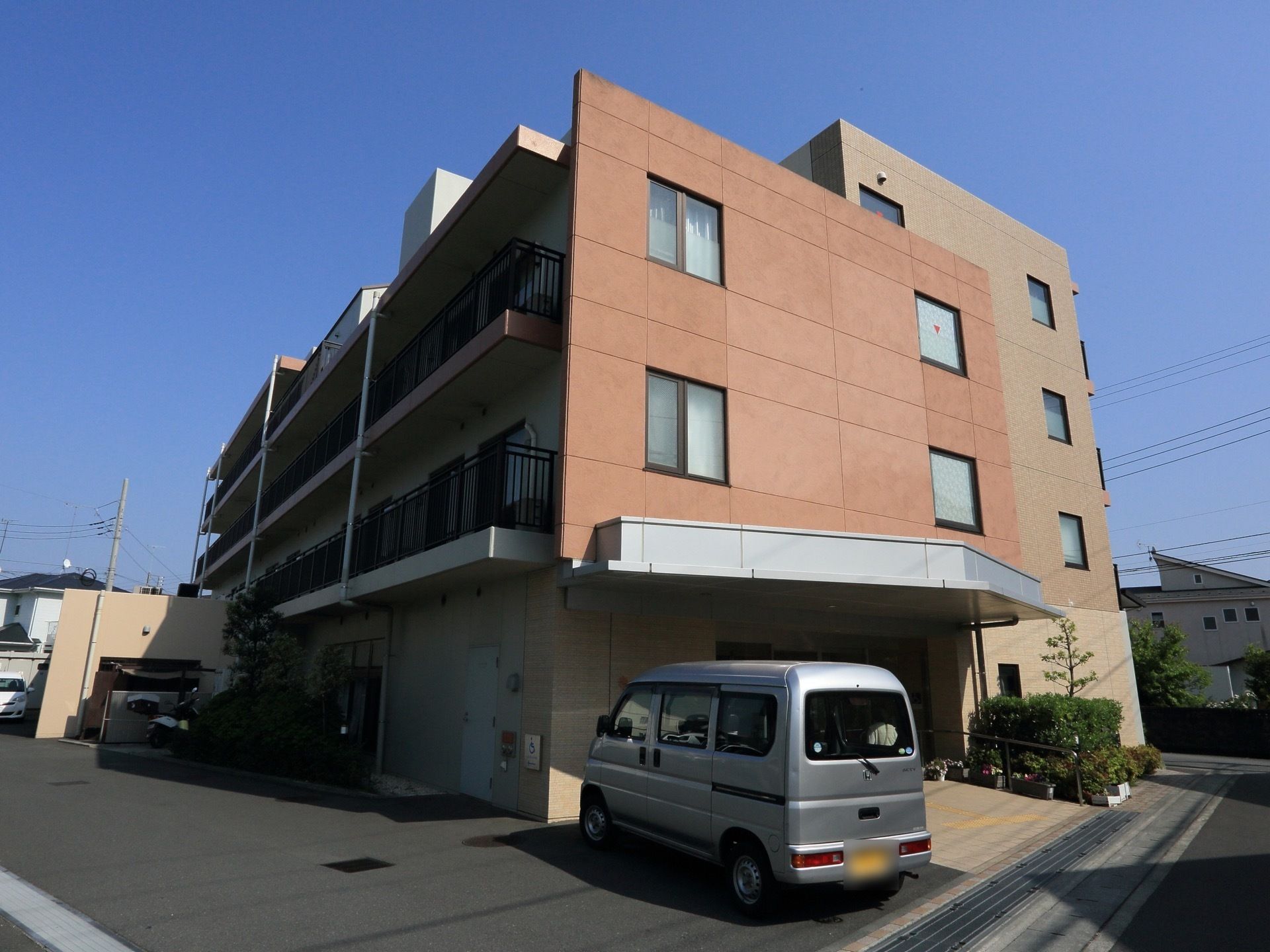 オレンジ色が特徴的な外観の施設である。道路から段差なく車でも出入りすることができる。周囲に木が植えてある。