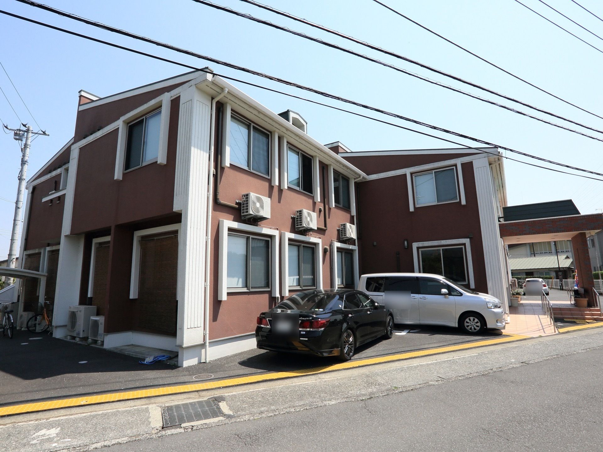 ２階建てで外壁は茶色と白で統一されている。建物の周りには駐輪場や駐車場があり、玄関はスロープとなっている。