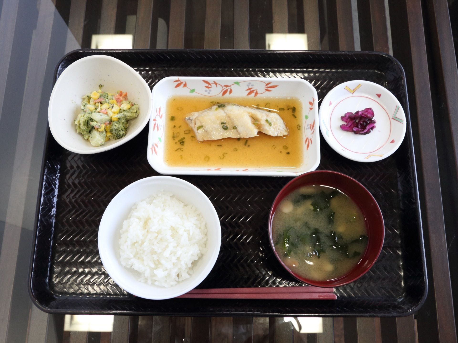 黒いお盆の上にごはん、味噌汁、副菜、メインディッシュ、漬物が置いてある。副菜は食べやすいように小さく刻んである。