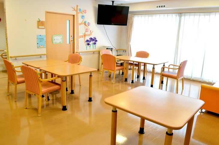 明るい光の差し込む、広い空間の共有スペース。入居者様がスタッフとともにレクリエーションを楽しんでいる。
