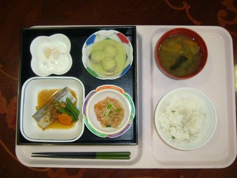 煮魚や小鉢、デザートの乗った黒い盆に、ご飯と味噌汁が添えられた食事用のプレート