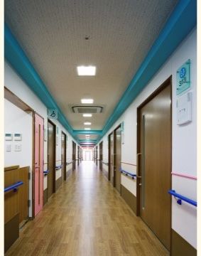 長い通路の両側の壁に手すりが設置され、各居室のスライドドアの扉が並んでいる。天井に照明と業務用エアコンが取り付けられている。