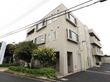 外観の左部分には、施設名が書かれた看板が立っている。入り口部分には大きな緑の木々がそびえ立っている。