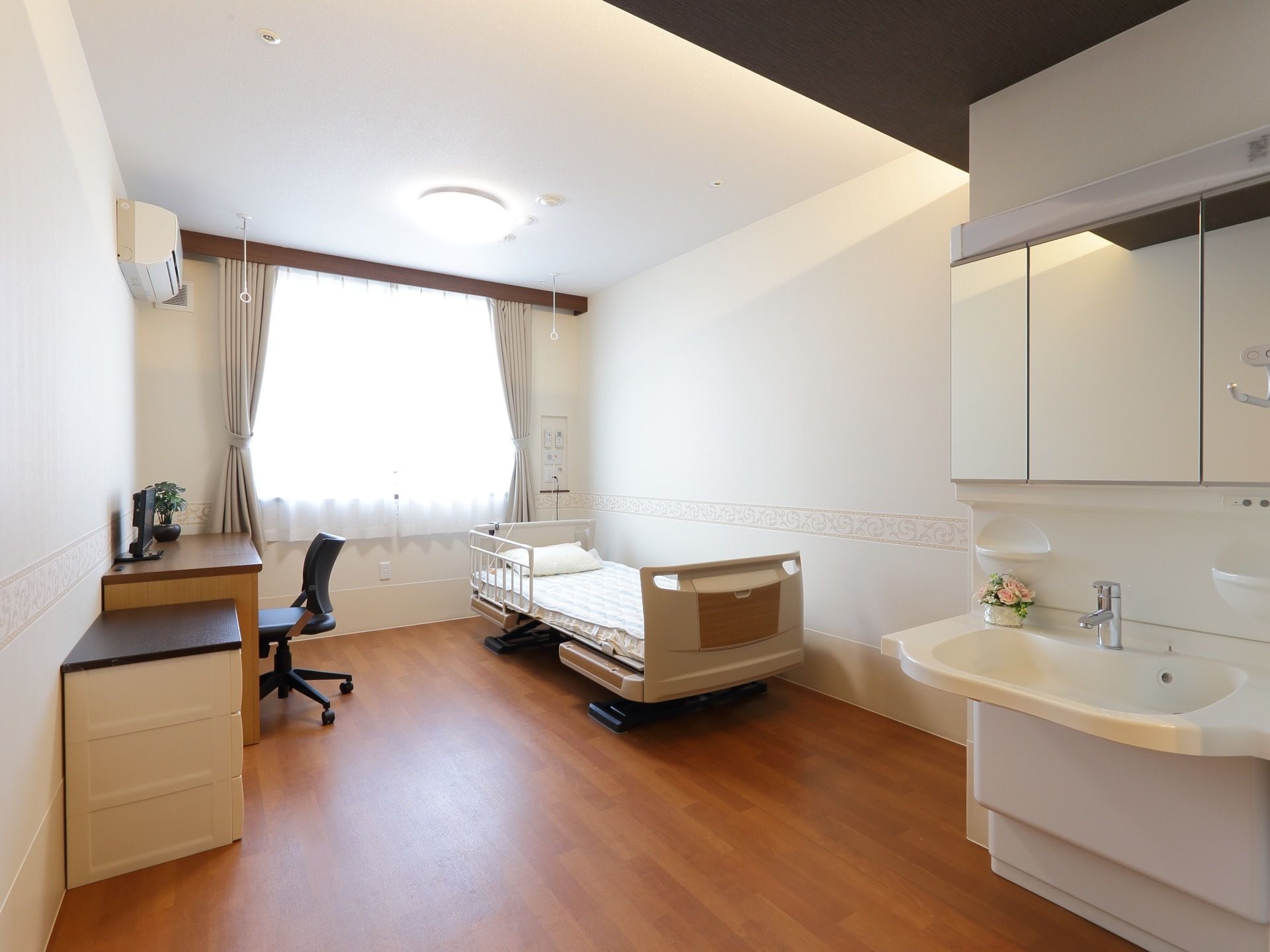 三面鏡付きの洗面台、ベッド、机や椅子などが置かれた部屋である。アクセントクロスや重厚感のあるカーテンレールなどラグジュアリーな空間である。