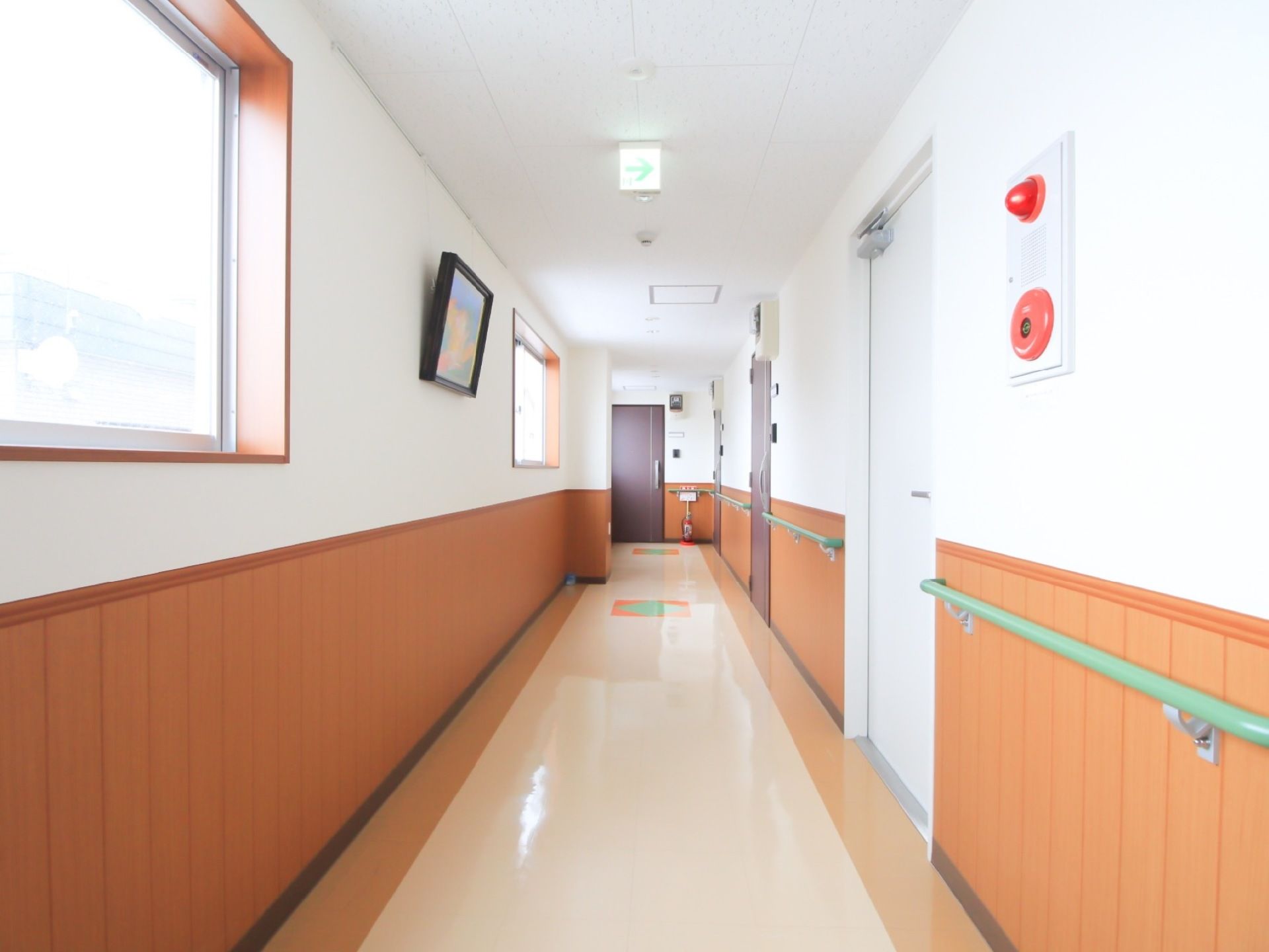 真っ直ぐと奥へ続く通路の左側上部には窓があり、右側には居室への扉が並んでいる。右側壁には、緑色の手すりが取り付けられている。