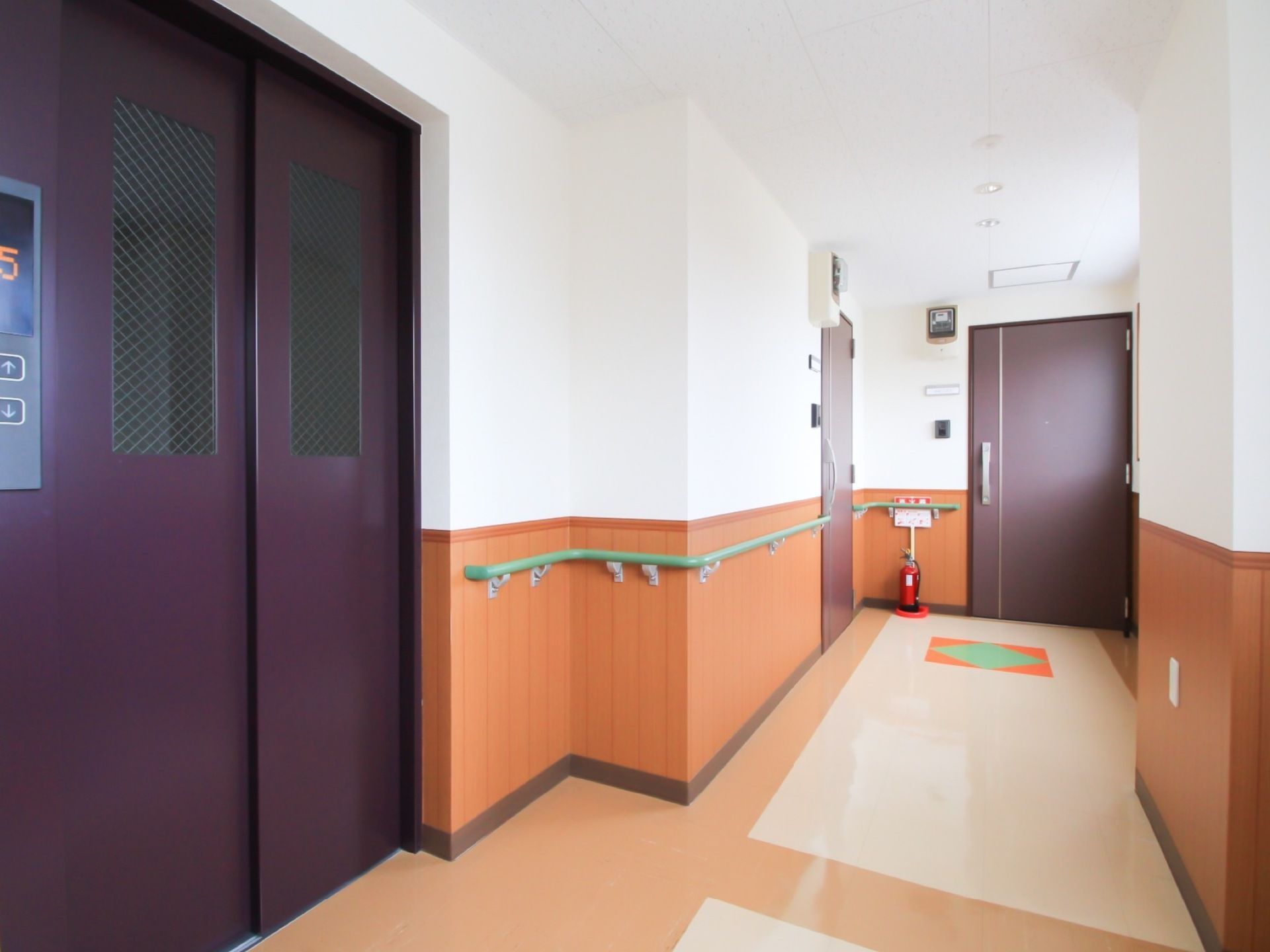 左側にはエレベーターの扉があり、画面奥には居室への扉がある。右側には窓があり、光が入って明るい空間となっている。