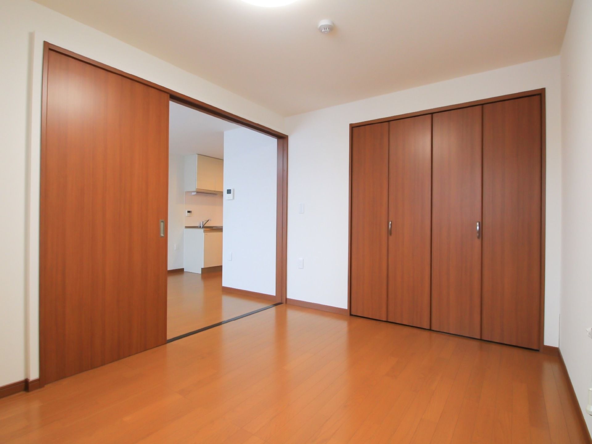 白と茶でまとめられたシンプルな居室である。奥にはキッチンがあり、手前の部屋にはクローゼットがある。部屋の扉は大きな引き戸である。