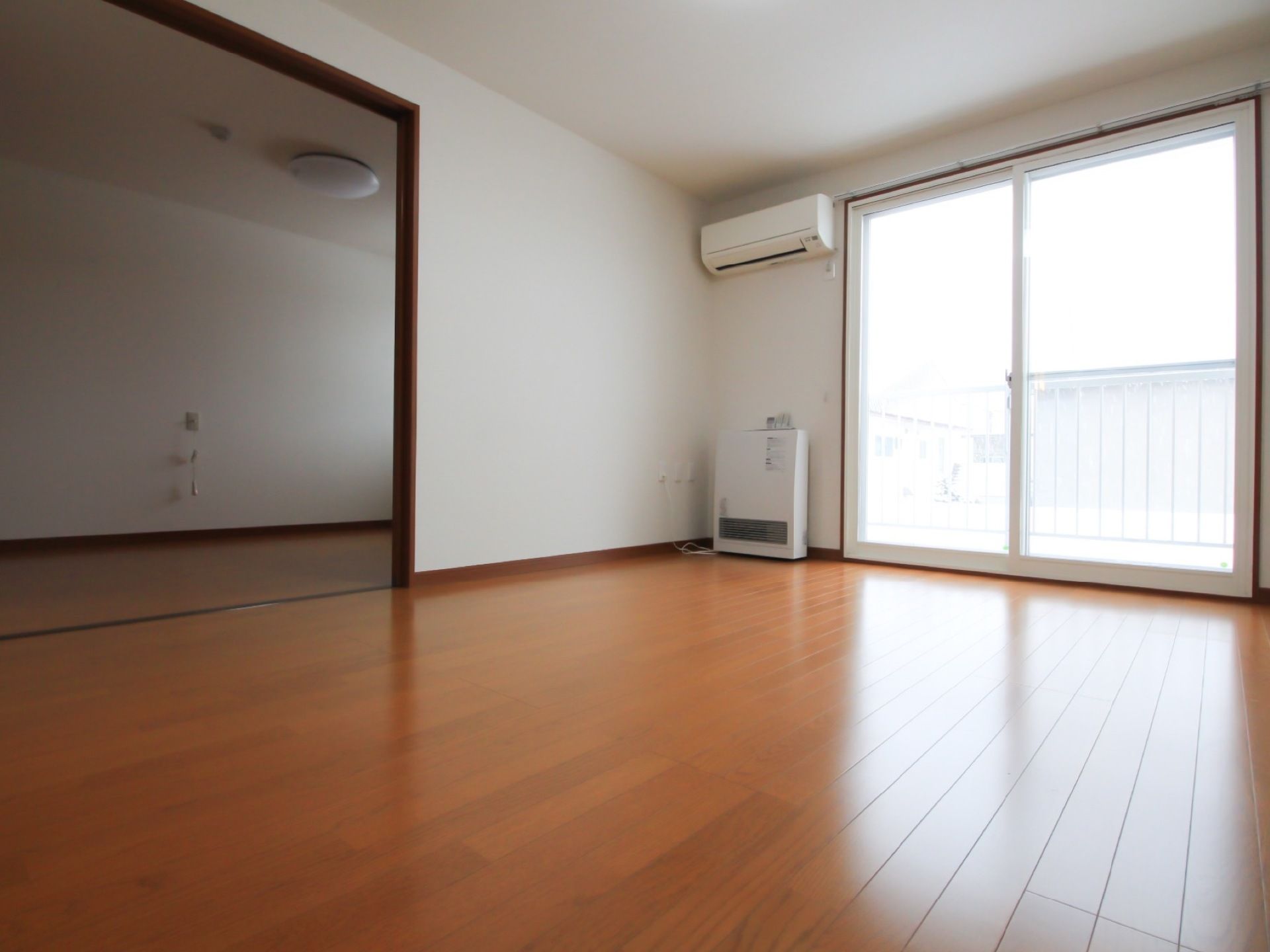 白と茶色を基調とした居室が２部屋に区切られている。右側には大きな窓があり、上部にはエアコンが取り付けられている。