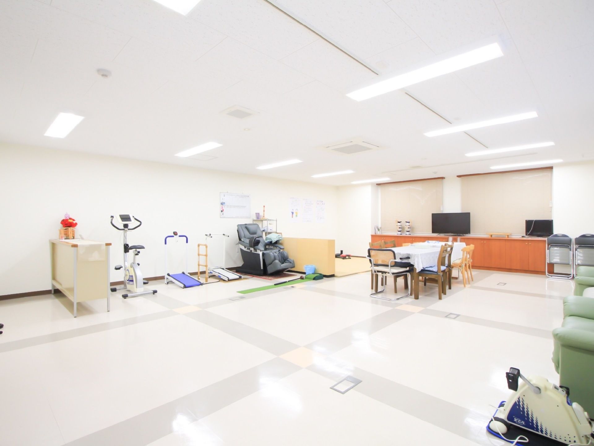 白を基調とした、広々とした空間である。奥にはテレビ、テーブルがある。壁際にはフィットネスマシーンやマッサージチェアが設置されている。