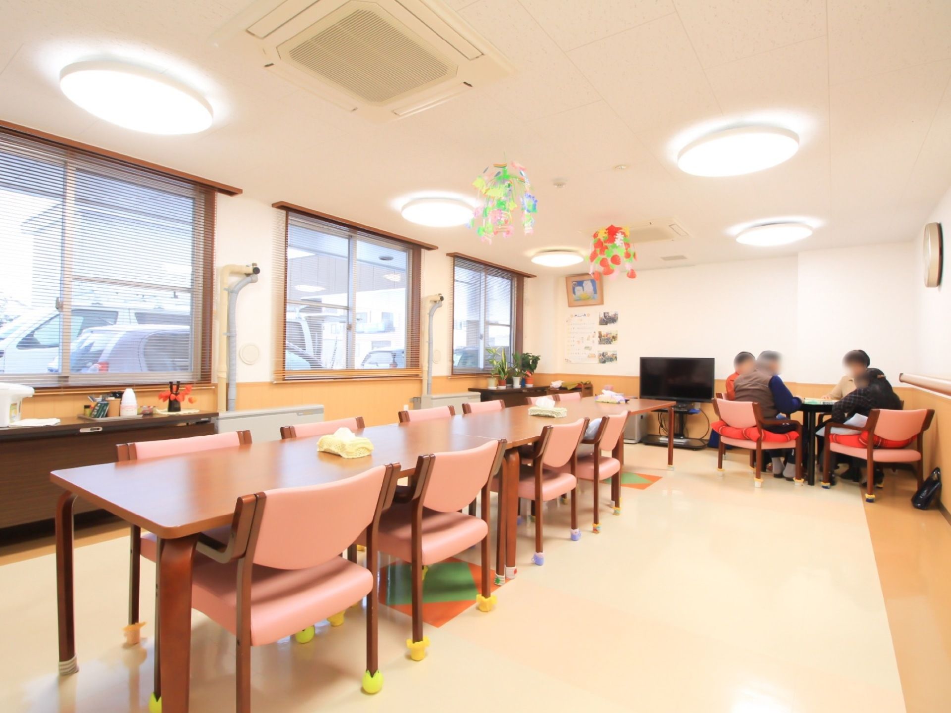 ダイニングテーブルがある。テレビが設置されており、入居者様が椅子に座って思い思いに過ごしている。