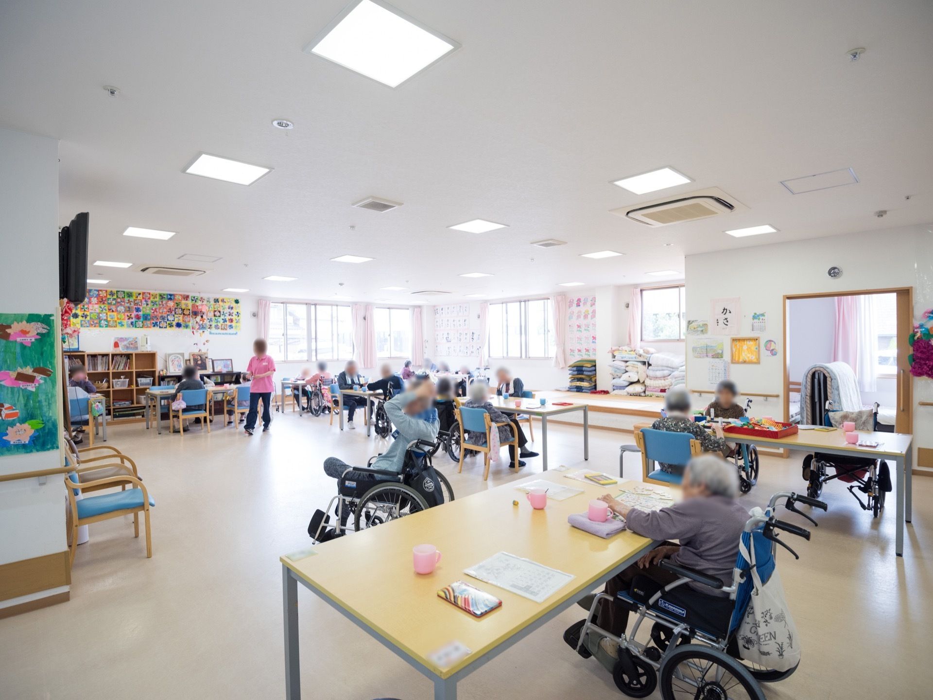 広々とした共有スペースにはいくつかのテーブルと椅子が設置されており、入居者様が談笑や塗り絵を楽しんでいる。