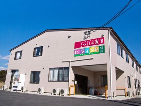 明るいグレーの壁に黒い切妻屋根で、入り口わきに自動販売機が置かれている建物