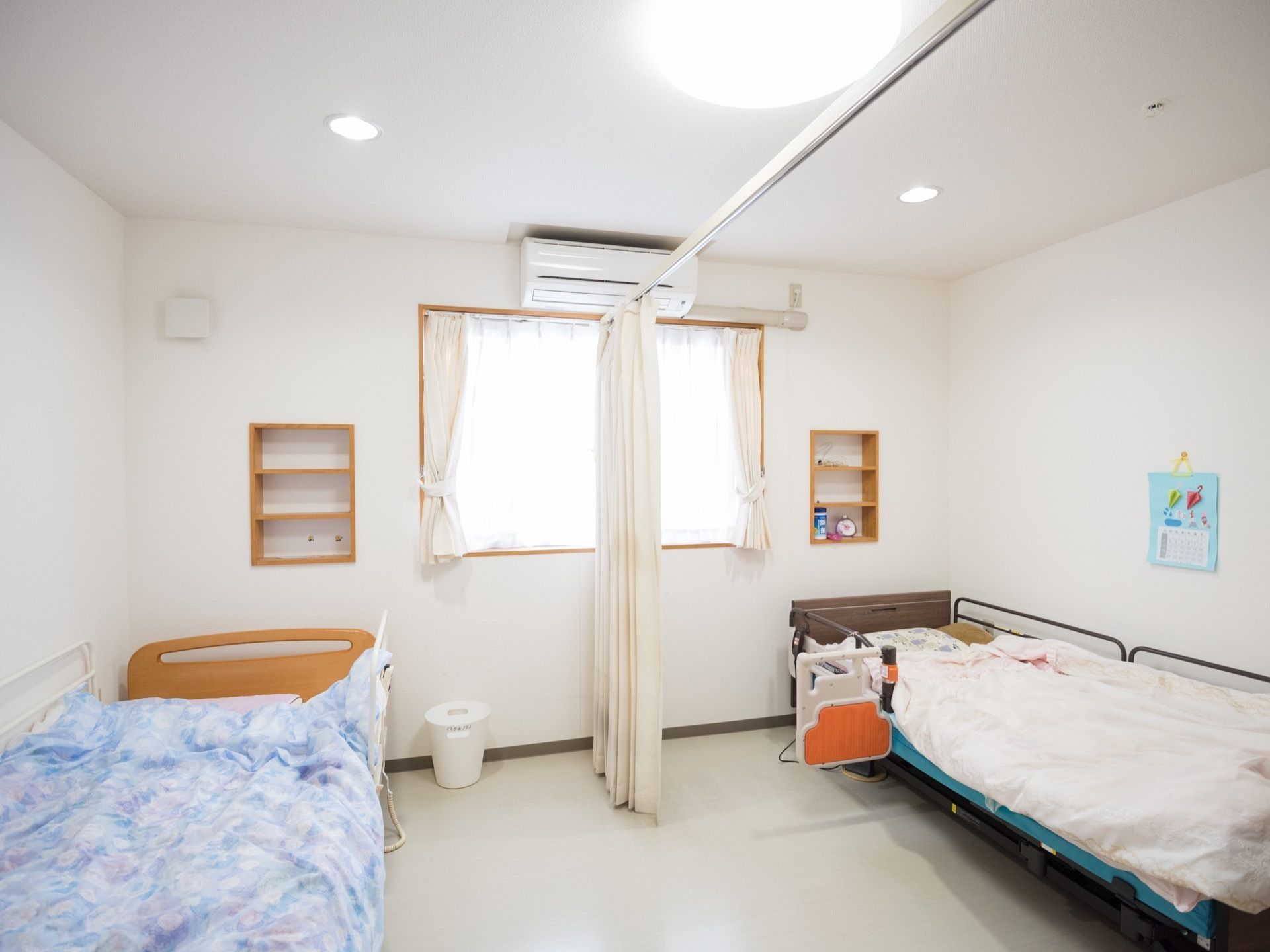 居室内中央がカーテンで仕切られていて、それぞれベッドが一台ずつ置かれている。エアコンが設置されている。