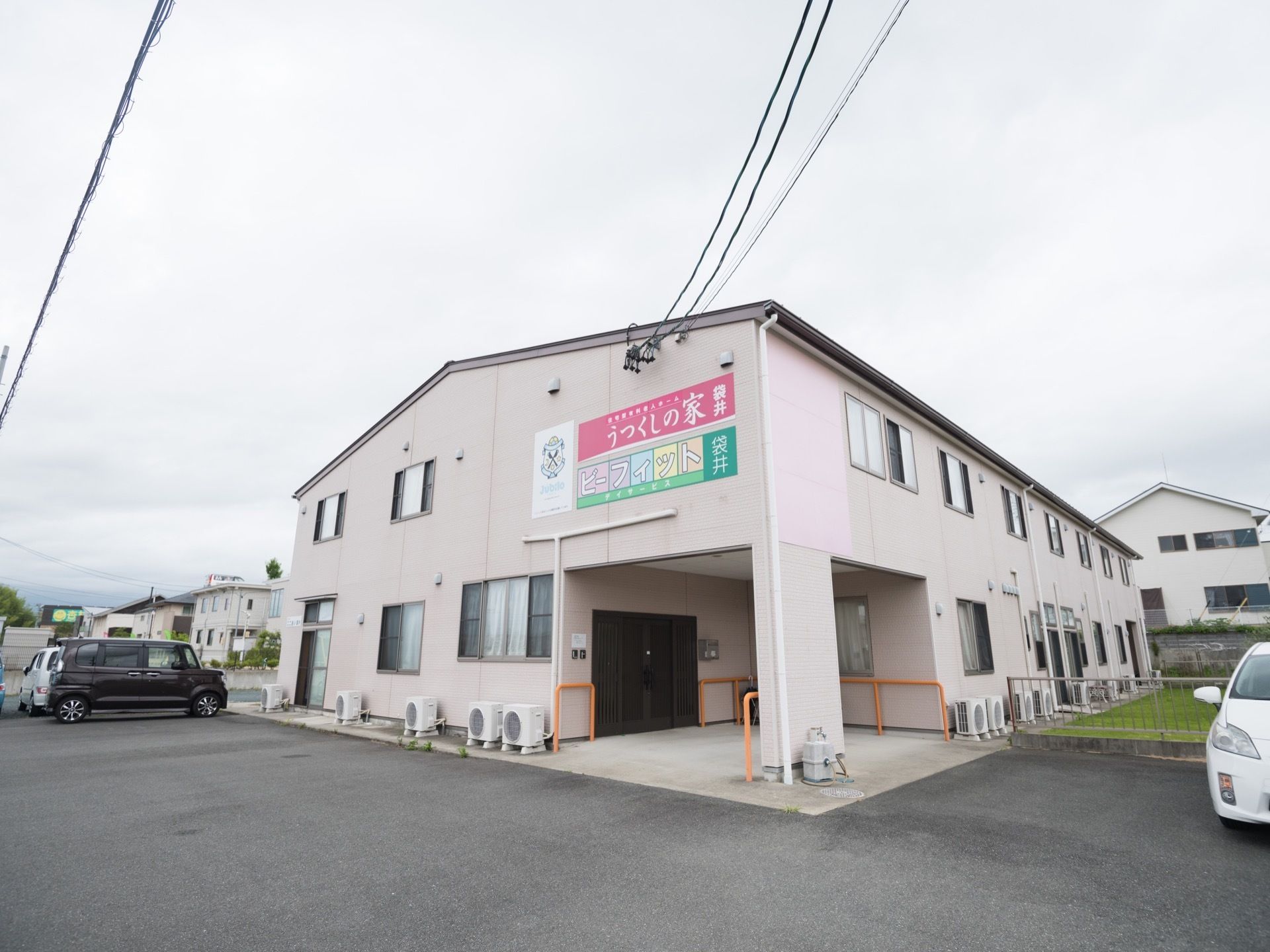 白い外壁のシンプルな建物が建っている。敷地はアスファルトで舗装されていて、広い駐車スペースになっている。