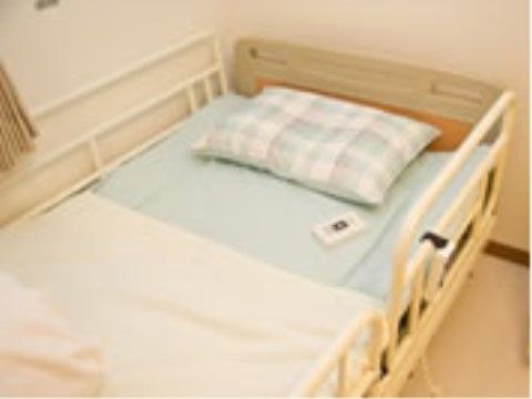 白っぽい壁にベージュの床、濃いベージュのカーテンの部屋に置かれたベッド