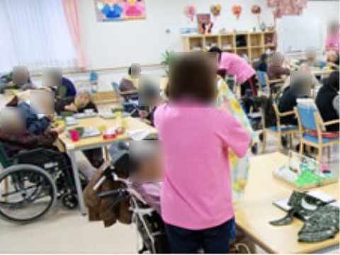 ピンクのシャツを着たスタッフと、食事の介助を受けている車椅子を利用する入居者様
