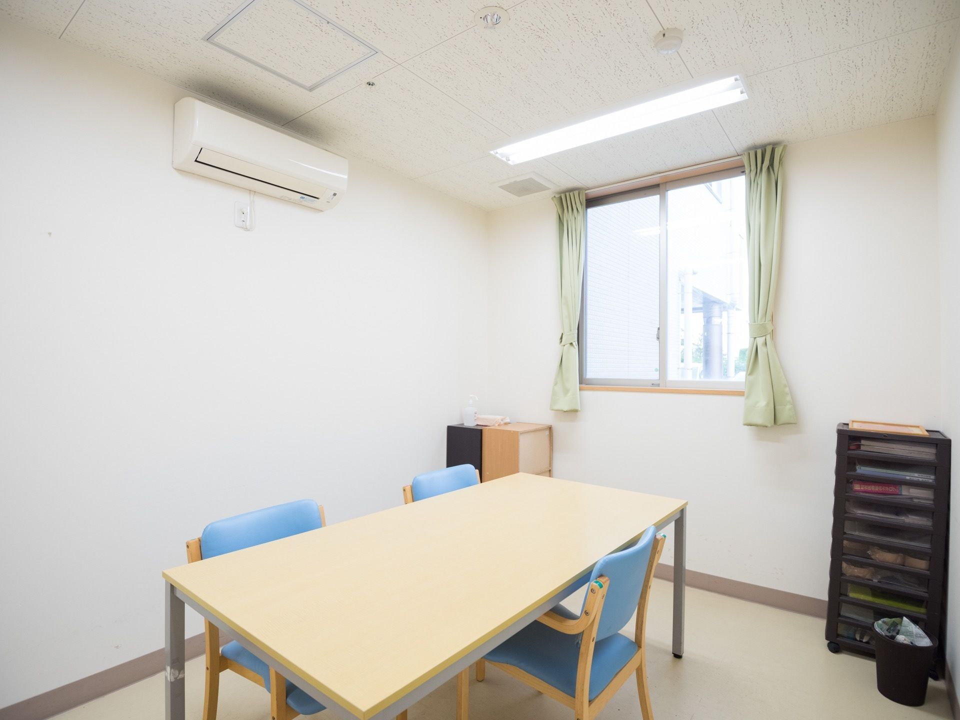 白が基調の明るく日当たりのよい相談室である。エアコンやテーブル、ひじ掛け付きの椅子、書類収納棚が完備されている。