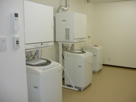 洗濯機と乾燥機が置かれ、手前の壁にコントローラーや呼び出しベルがある洗濯室