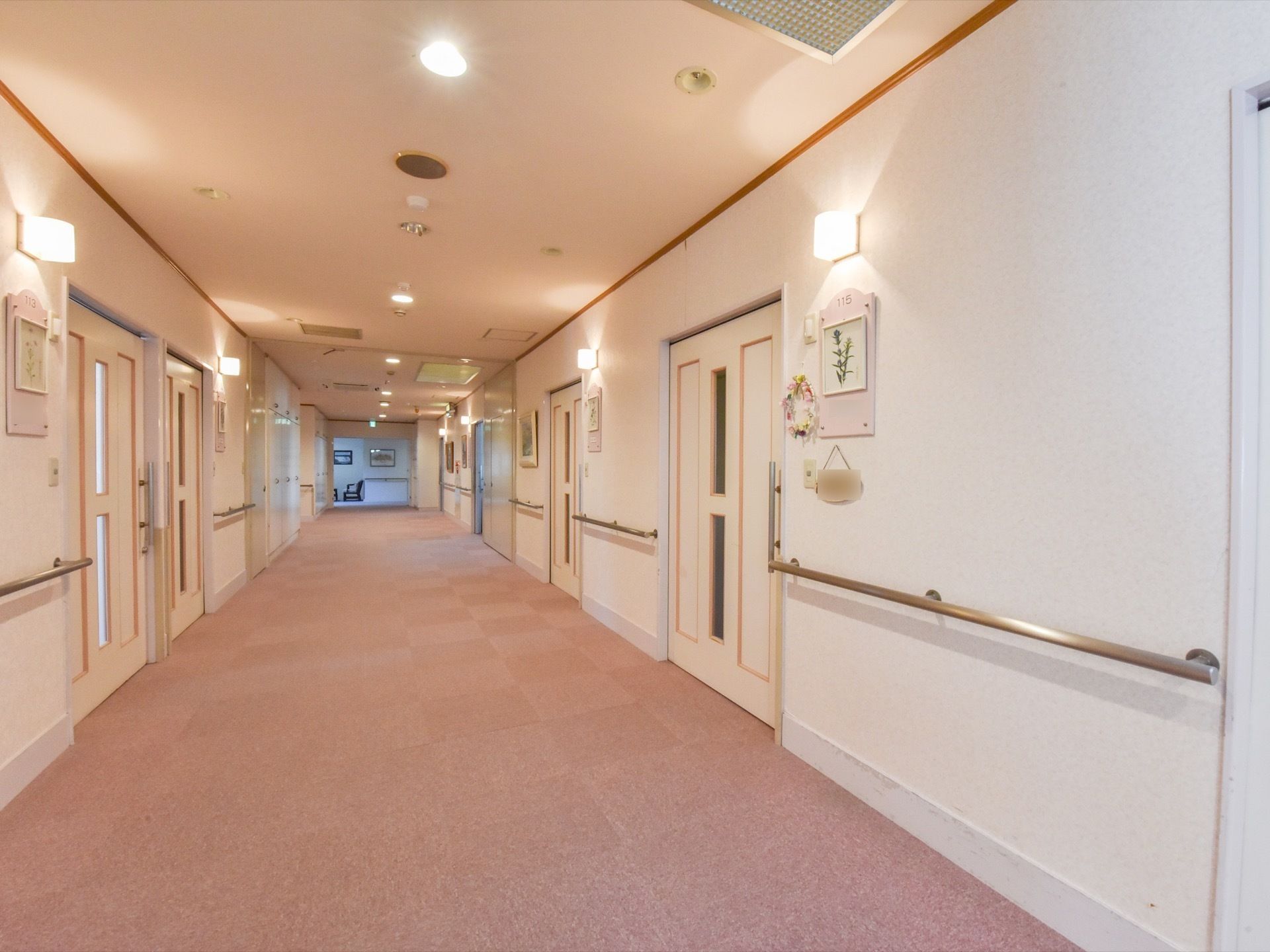通路には手すりが完備されている。居室のドアは引き戸になっている。部屋番号の下に花の絵が飾られている。
