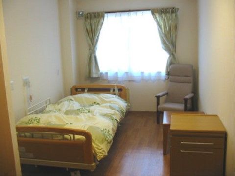 白い壁にフローリングで、奥に窓がありその手前にベッドが置かれた居室