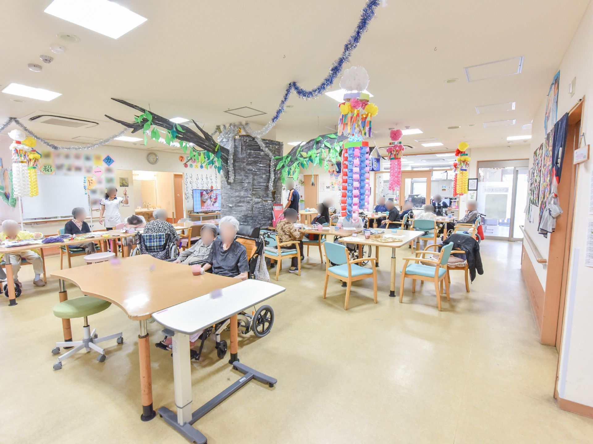 食堂には手作りの七夕飾りが天井から吊り下げてある。十数名の施設利用者が椅子にこしかけて、寝たり、お話したりして過ごしている。
