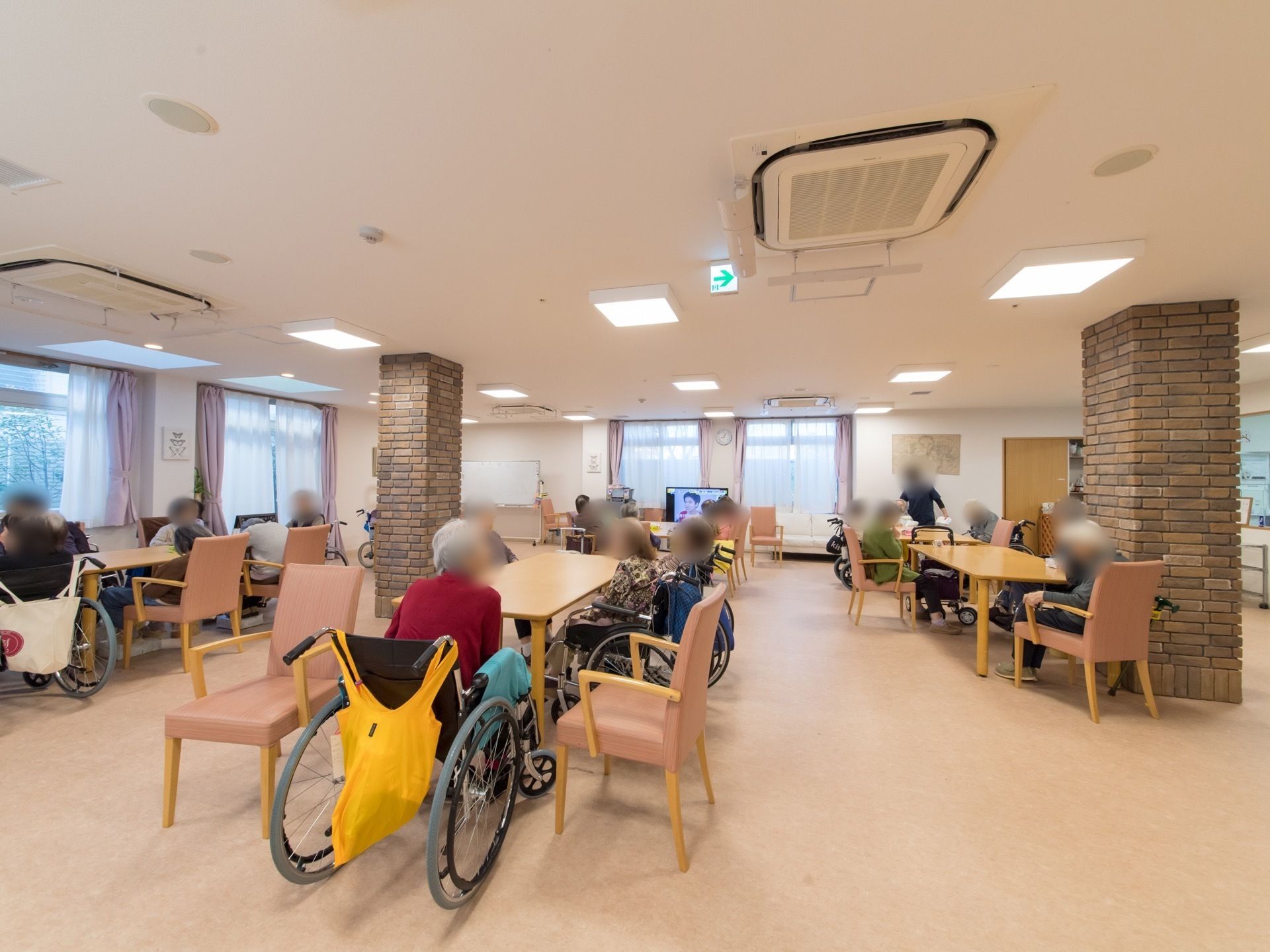 窓が沢山ある。テレビとホワイトボードが置いてある。椅子と机が沢山置いてあり大人数で食事が取れる。机の間のスペースが広い。