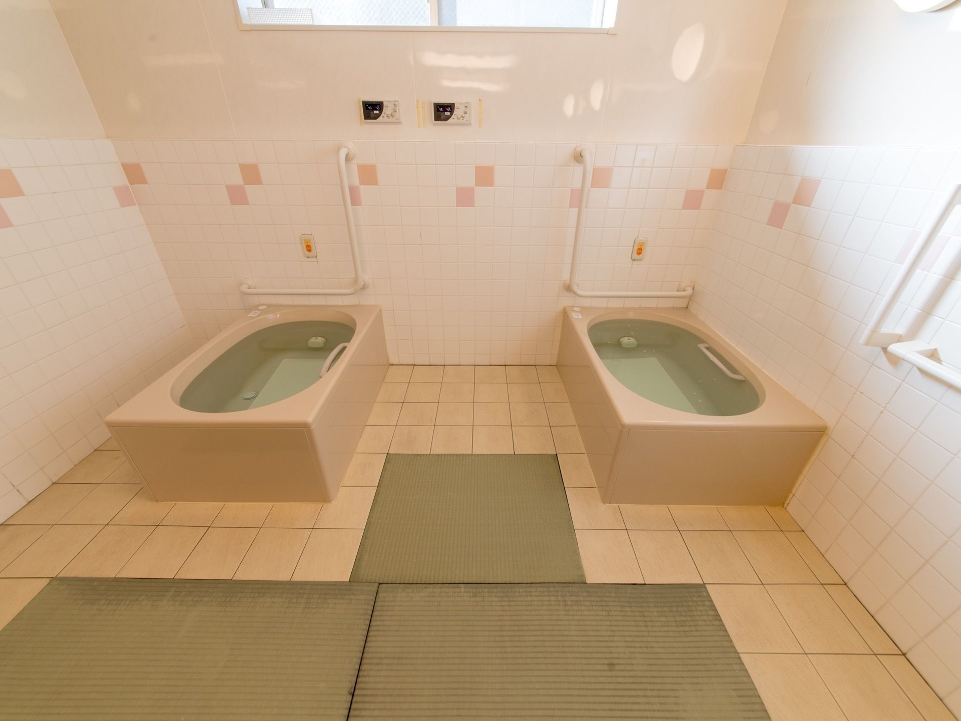 大きめのバスタブが2つ置かれている。滑り止めのマットが敷かれている。ナースコールと手すりが設けられている。