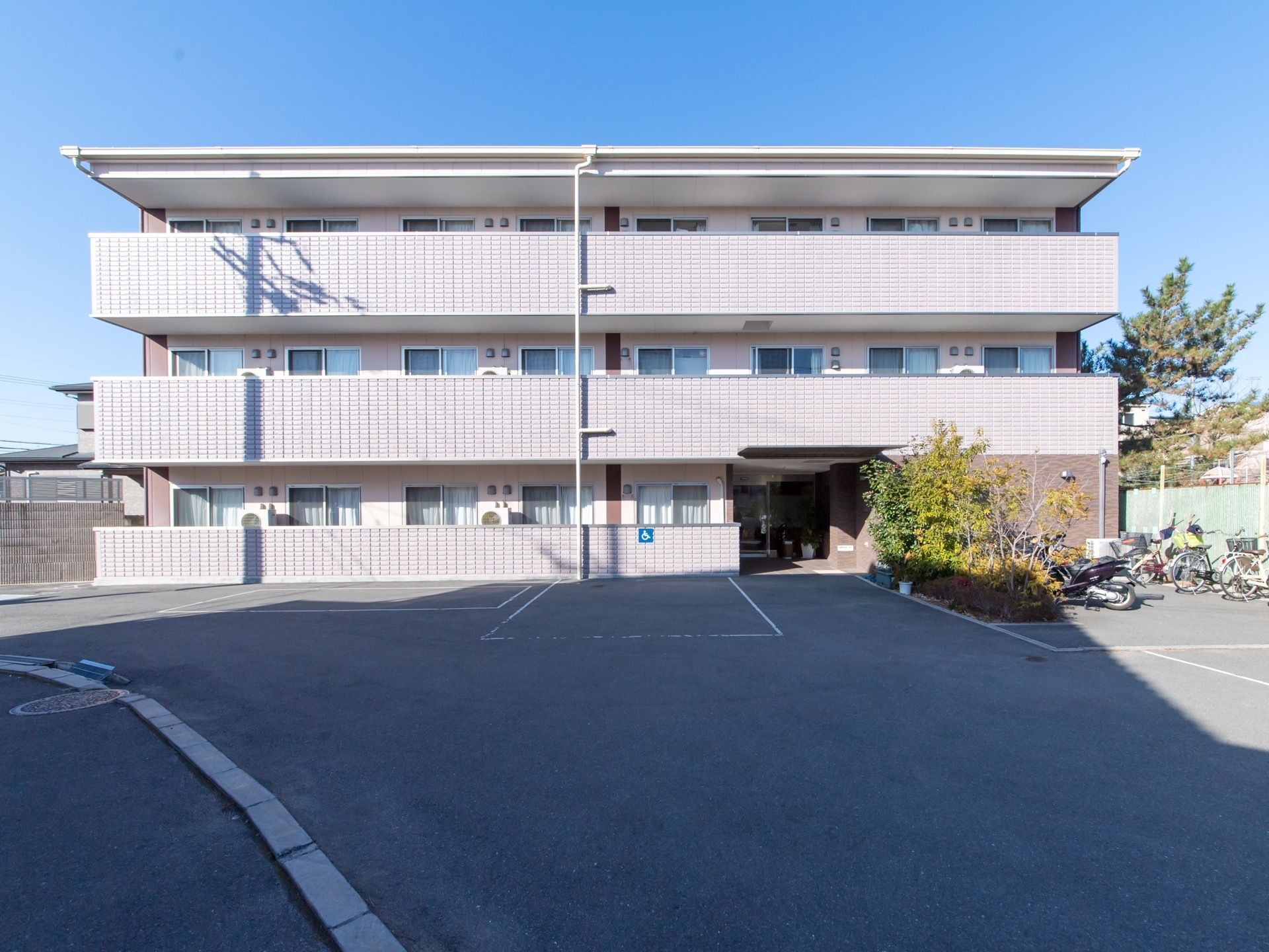 施設は３階建てである。敷地内に駐車場がある。玄関にむかって右側に植え込みがあり、その横に駐輪場が設置されている。