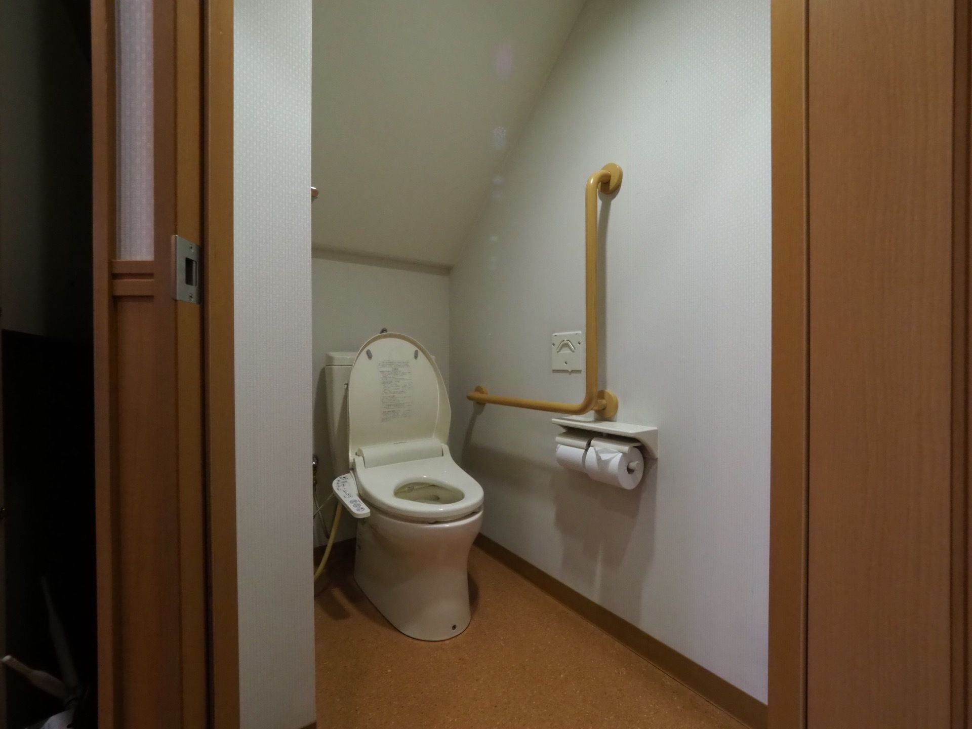 清潔感のあるトイレで、白い壁と茶色の床になっている。温水洗浄便座で使いやすい。壁には手すりが設置されている。