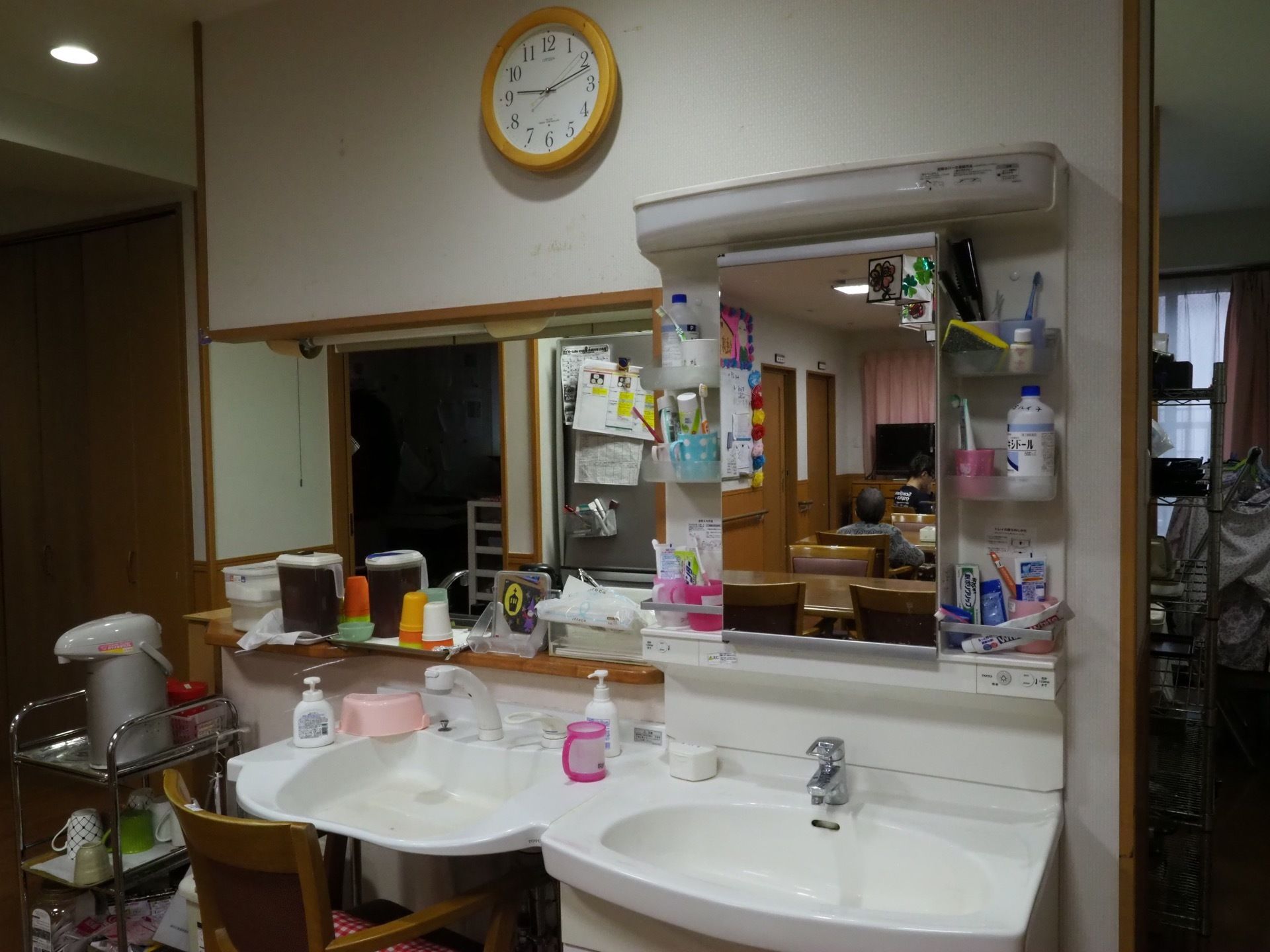白い壁に時計が設置され見やすくなっている。洗面台の前にはイスがあり、座って利用することができる。ペーパータオルがあるので便利である。