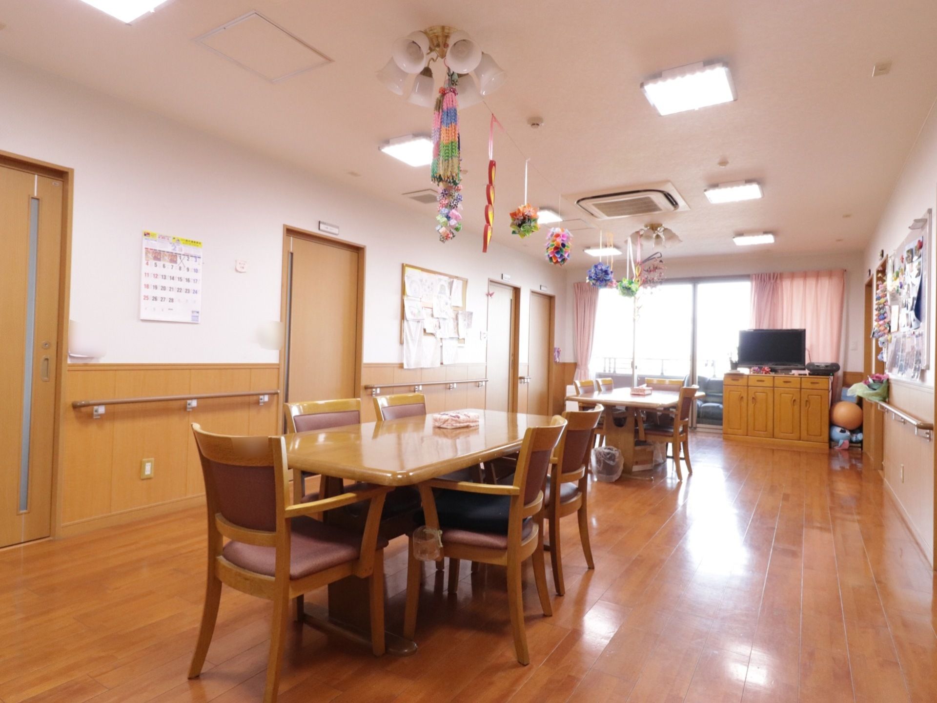 清潔感のある明るい食堂である。大型液晶テレビやソファ、掲示板、テーブルセット、手すり、エアコンが完備されている。