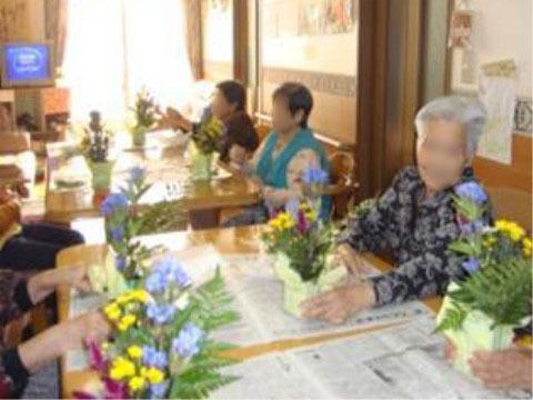 2つのテーブルに座って、花のアレンジメントをする数人の高齢者