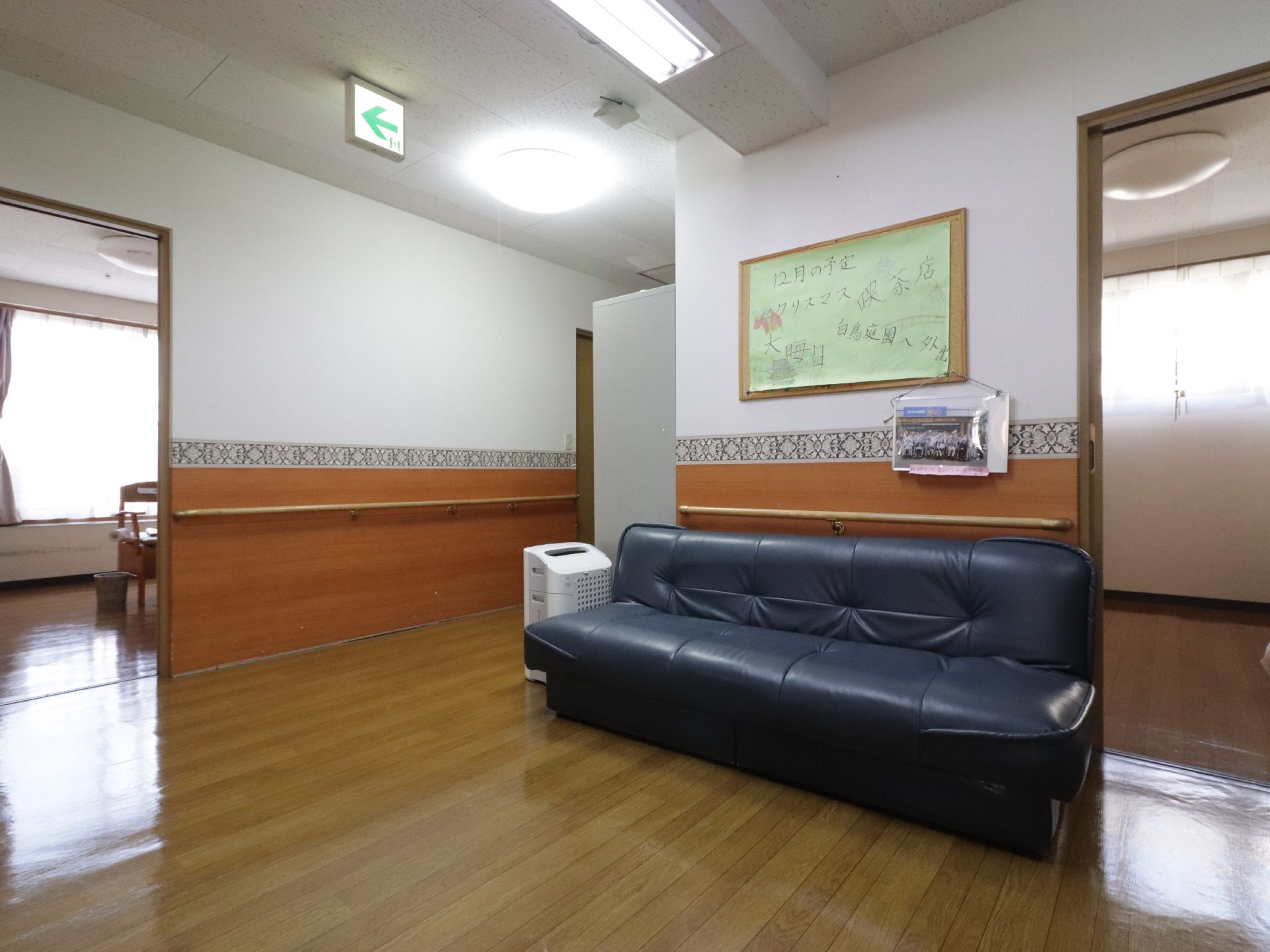 通路の一角には3人ほどが座ることができるソファーが置かれている。後ろ側の壁には12月の予定が書かれている。また、集合写真も貼られている。