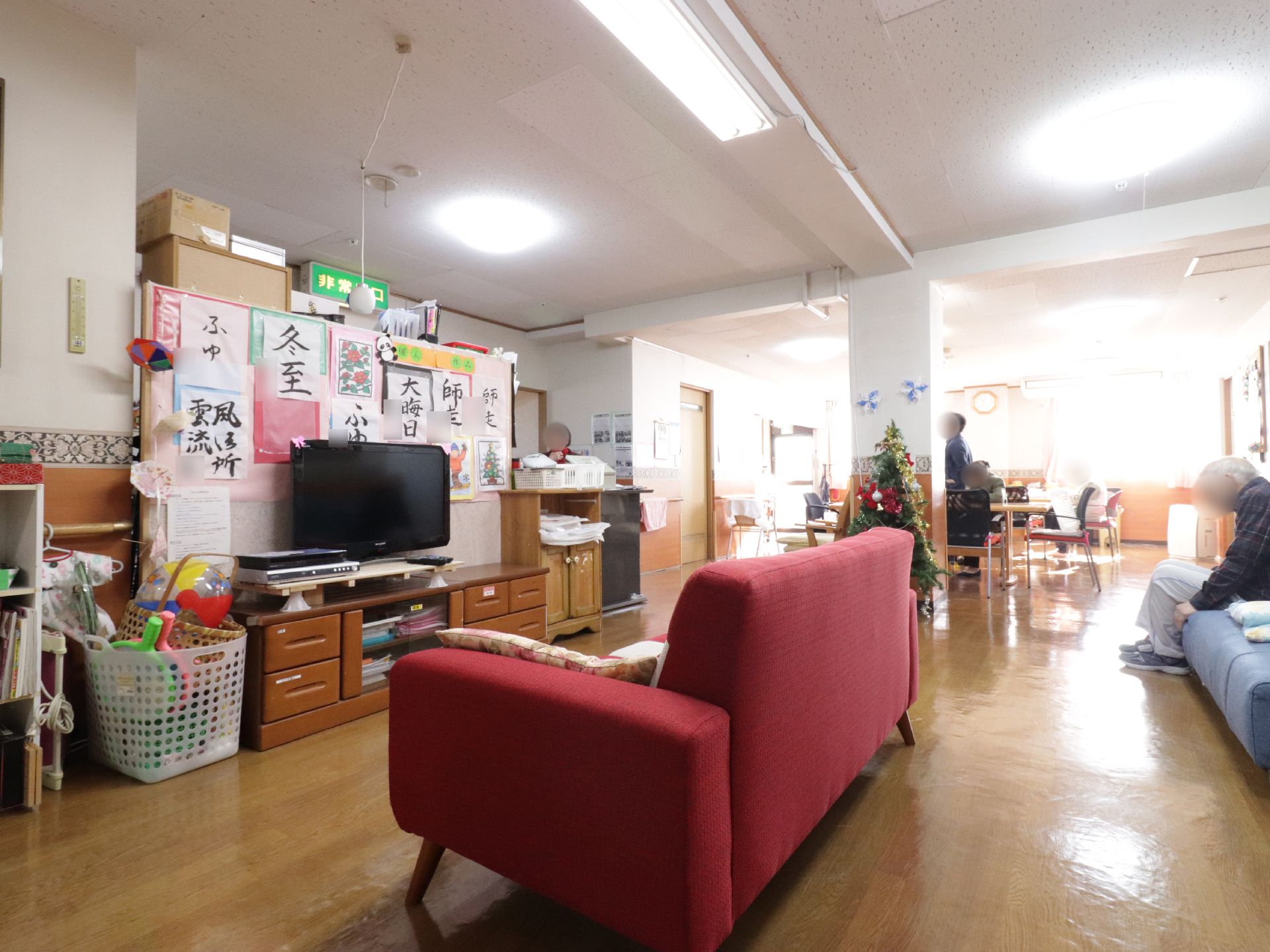 リビングにはテレビが1台設置されている。テレビの前には赤色と青色のソファが並べられている。青いソファーには入居者様が座っている。