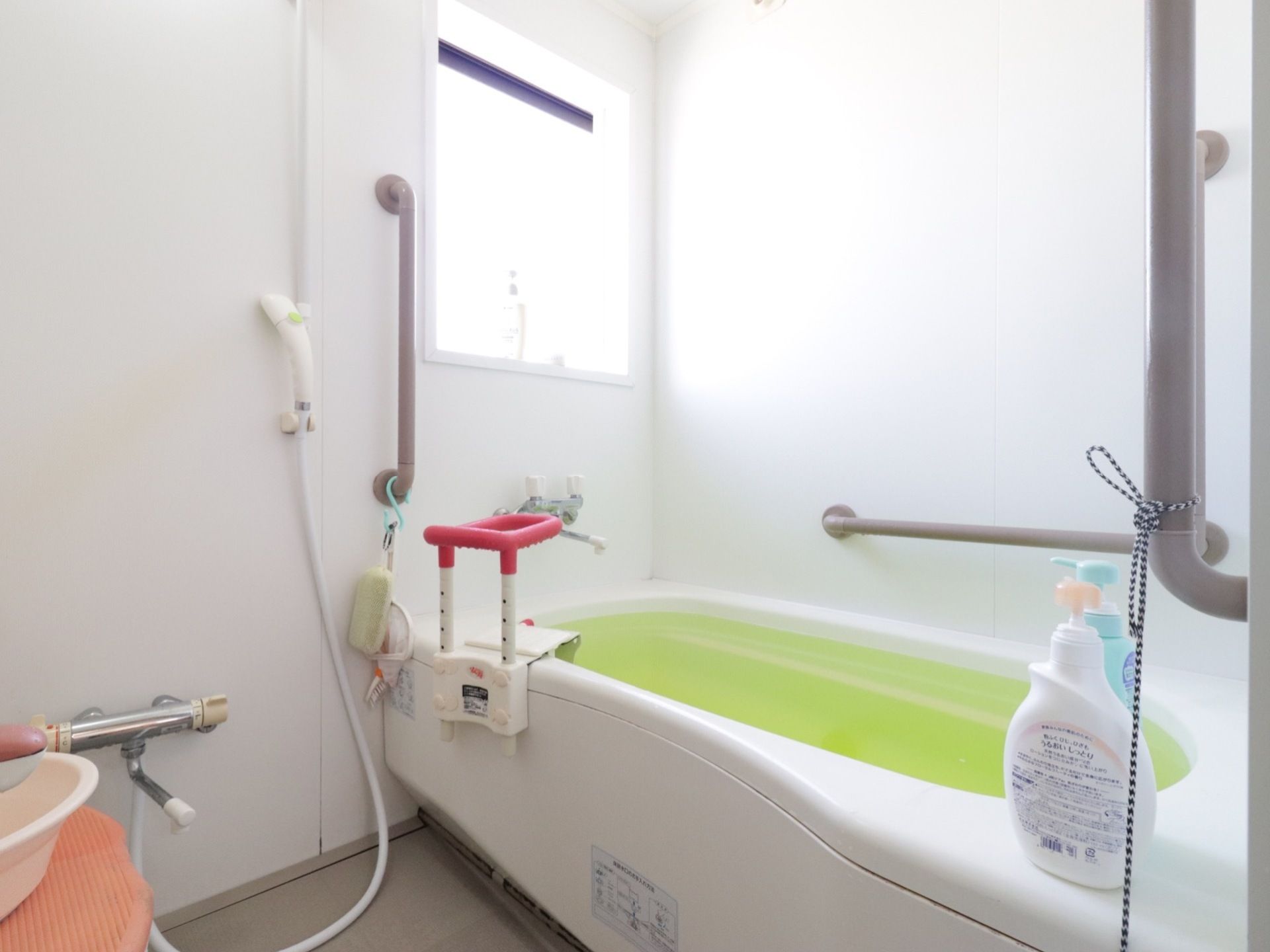浴室には窓がある。壁には縦型と横型の手すりがあらかじめついている。浴槽には後付けされた手すりも取り付けられている。