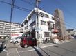 施設は3階建てで白い外観である。入り口近くには駐輪場と駐車場があり、自転車と車が数台止められている。