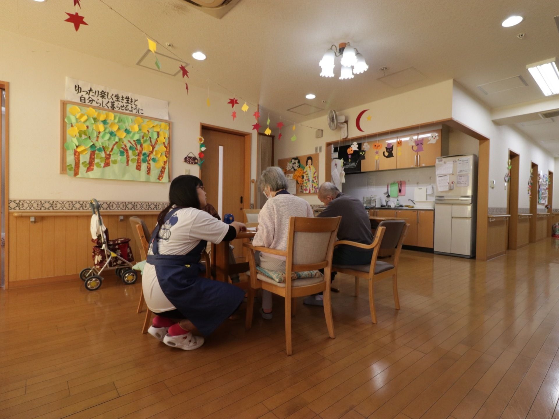 壁には施設からのメッセージと貼り絵が飾られている。キッチンの横に木製のテーブルと椅子が置かれている。