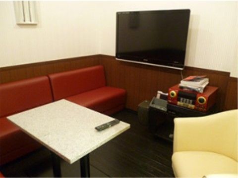 壁に大型のモニターがあり、右側にカラオケの機材、左の白いテーブルにマイクが置かれたカラオケルーム