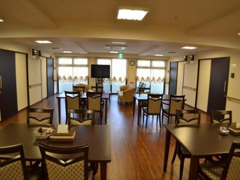 居室前に設けられた開放的なリビングである。食卓の隣には、ソファーやテレビが置かれた休憩スペースがある。