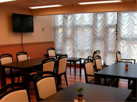 窓に大きなドレープの付いたカーテンがかかり、茶色のテーブルに白い背もたれの椅子がセットされた食堂