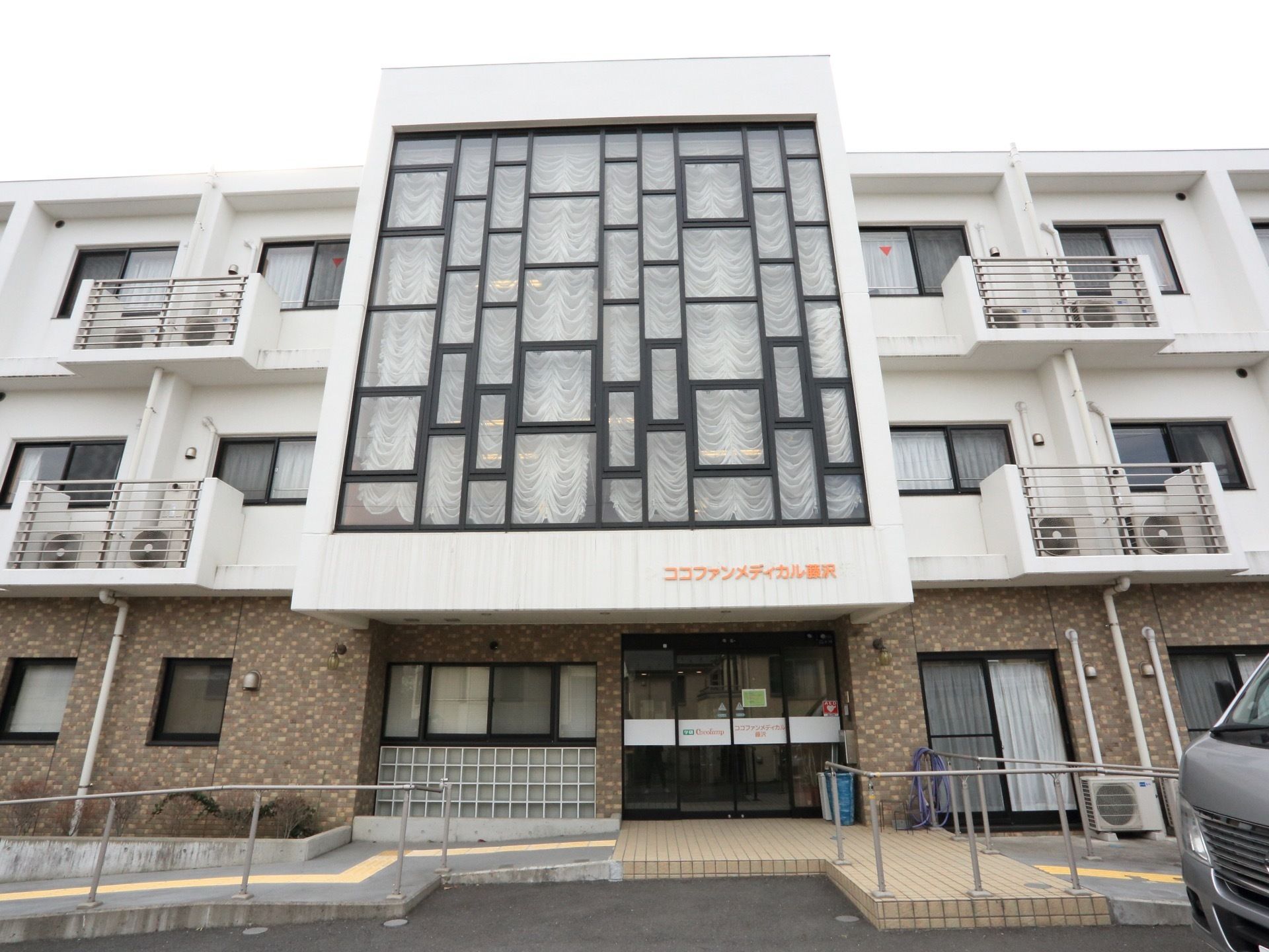 特徴的なデザインの窓がある施設は３階建てになっている。施設前にスロープを設置しており車椅子をご利用の方が安全に移動できる。