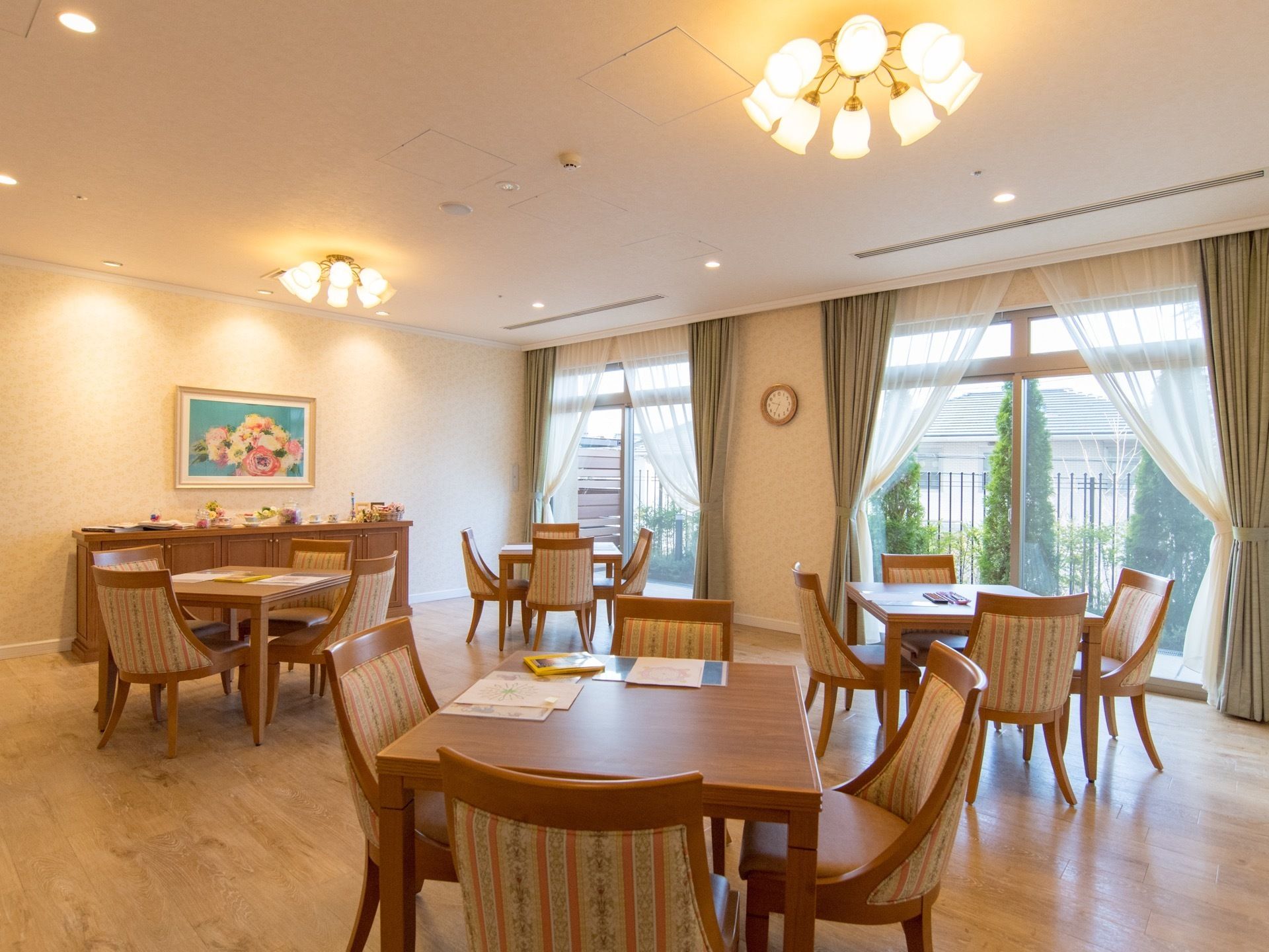 部屋には４台のテーブルにそれぞれ４脚ずつ椅子が設置されている。大きな窓があり、カーテンが二重にかかっている。壁には絵が飾られている。