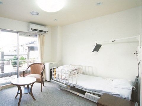 左側に大きな窓、その前に一人用のテーブルセット、右側にベッドの置かれた居室
