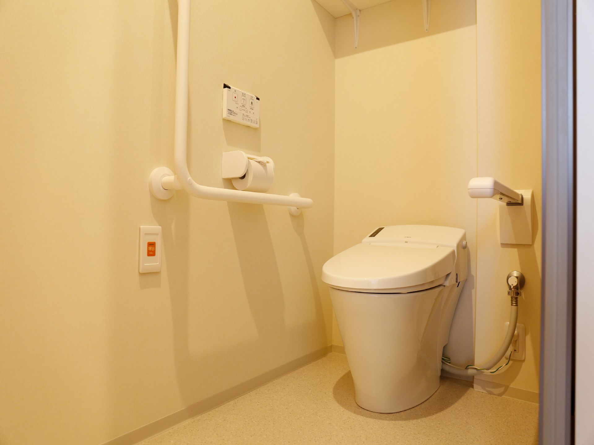 居室のトイレは左右両側に手すりのついた洋式トイレで、引戸つきの個室である。右側の壁にトイレ操作と呼び出しのボタン、ペーパーホルダーがある。