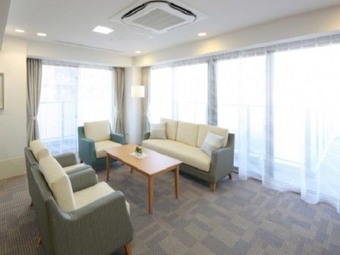 白地のカーテンや、グレーを基調としたソファで整えられた落ち着いた空間である。横長のソファの両端には、小さなクッションが添えられている。