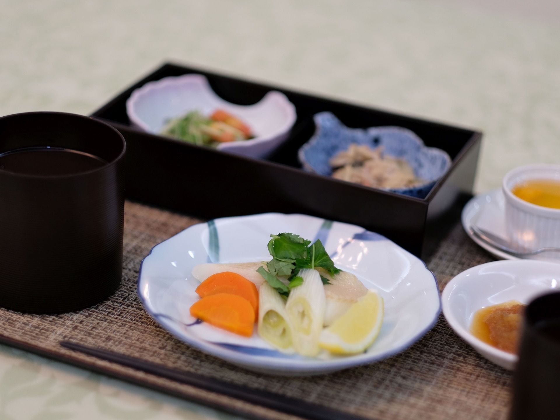 汁物とメインディッシュ、副菜でそれぞれ食器が分けられている。副菜は容器の上に小鉢が２つ置かれている。